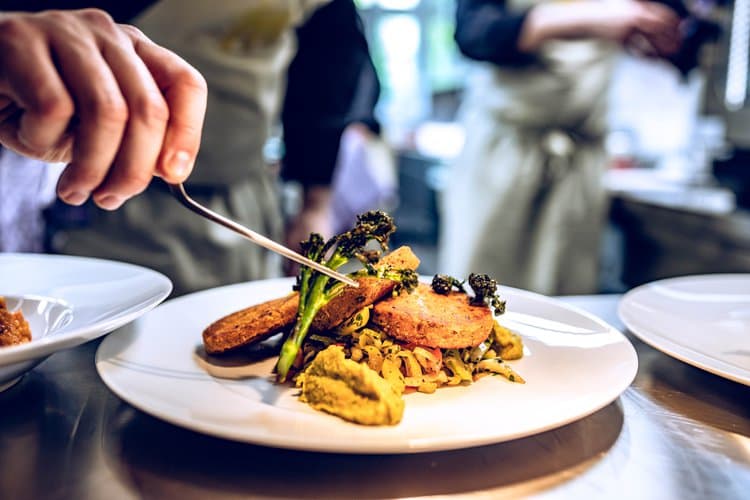 Kochsternstunden Schleswig-Holstein: Koch richtet raffiniertes Brokkoli-Gericht auf weißem Teller kunstvoll an.