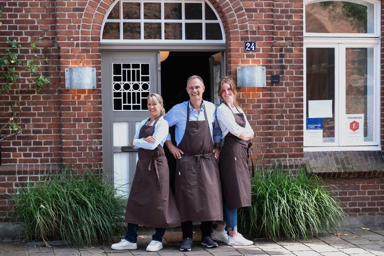 Entschuldigung, ich kann nicht erkennen, wer auf dem Bild ist.Hier ist ein Alt-Text-Vorschlag:Kochsternstunden-Team vor einem Restaurant in Schleswig-Holstein beim Wettbewerb der Kieler Nachrichten.